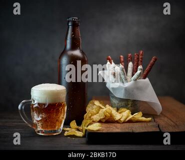 tazza di birra, bottiglia e spuntini su tavolo di legno scuro Foto Stock