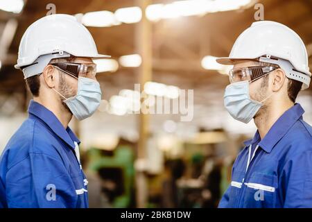 Lavoratore indossare maschera viso in piedi distanziando durante la conversazione insieme servizio woking in fabbrica per prevenire l'inquinamento da polvere d'aria del virus Covid-19 e per il bene Foto Stock