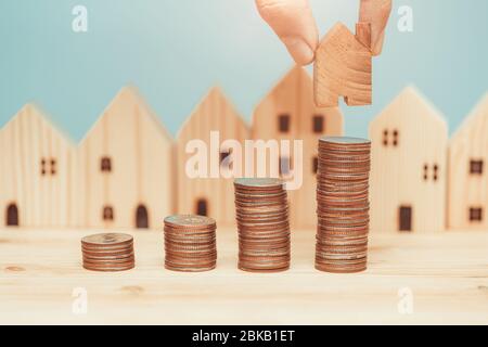 Pila di monete con modello domestico di legno per risparmiare i soldi per comprare un nuovo concetto domestico. Foto Stock