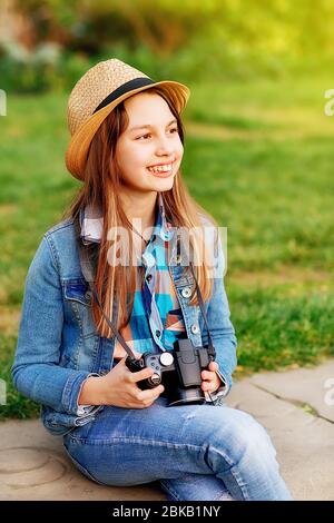 Ragazza che indossa un cappotto in denim, una sciarpa arancione e jeans che cammina per il centro della città, scattando foto e porta un orso giocattolo sulle spalle Foto Stock