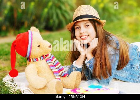 Ragazza che indossa un cappotto in denim, una sciarpa arancione e jeans che cammina per il centro della città, scattando foto e porta un orso giocattolo sulle spalle Foto Stock