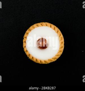 Vista dall'alto primo piano di UNA torta Bakewell appena sfornata con un unico Ciliegio glassato, isolata su uno sfondo nero senza persone Foto Stock