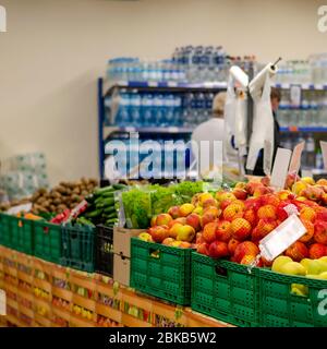 Bancarelle con frutta e verdura in un supermercato. Scatole di plastica riempite di mele, lattuga, cetrioli e altri alimenti. Silhouette sfocate di shopp Foto Stock