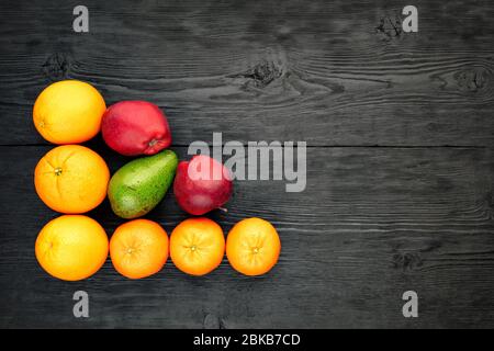 Arance, tangerini, mele e avocado giacciono su una vecchia superficie in legno nero, stile rustico, piatto, spazio copia. Foto Stock
