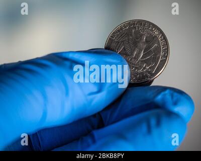 Una mano che indossa guanti di protezione blu che tengono una moneta da un quarto di dollaro. Foto Stock