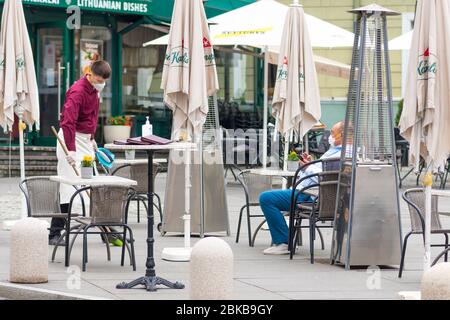 Il cameriere con maschera disinfetta il tavolo di un bar, caffetteria o ristorante all'aperto, riapre dopo le restrizioni di quarantena Foto Stock