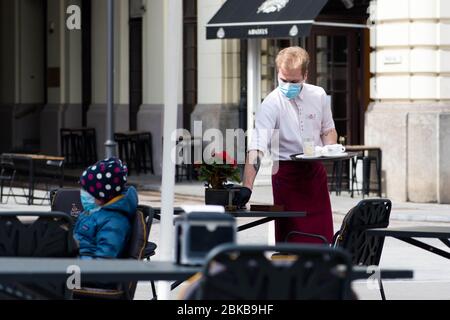 Il cameriere con maschera disinfetta il tavolo di un bar, caffetteria o ristorante all'aperto, riapre dopo le restrizioni di quarantena Foto Stock