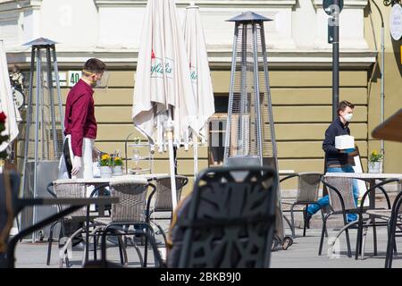 Il cameriere con maschera disinfetta il tavolo di un bar, caffetteria o ristorante all'aperto, riapre dopo le restrizioni di quarantena Foto Stock