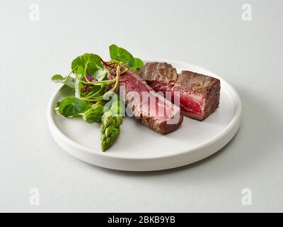 Piatto di carne di manzo wagyu con erbe e asparagi su sfondo grigio chiaro Foto Stock