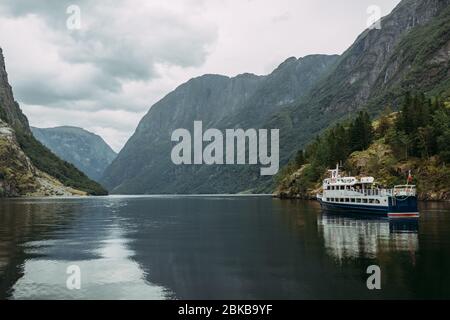 Nave turistica su un fiume di montagna sullo sfondo delle montagne norvegesi e il cielo coperto di conchiglie Foto Stock