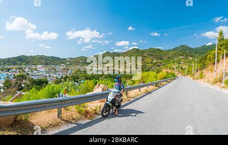Una persona in moto su strada tortuosa guardando la vista della splendida costa nella provincia di Phu Yen, Nha Trang Quy Nhon, avventura in Viet Foto Stock