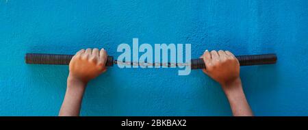 Nunchaku tenuta a mano isolata su sfondo blu. Nunchaku nero formazione per principianti. Equipaggiamento tattico caldo arti marziali. Foto Stock