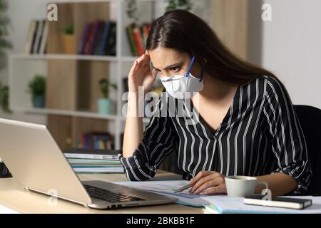 Donna imprenditore preoccupato che controlla il laptop e segnala di evitare covid-19 con maschera seduta su una scrivania a casa di notte Foto Stock