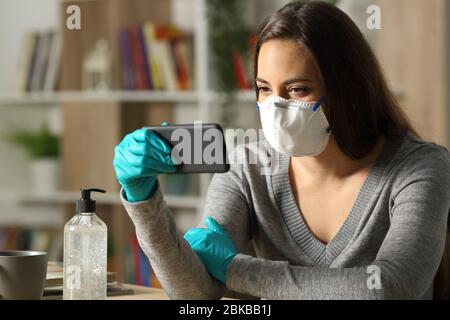 Donna che guarda video su smartphone su coronavirus confinamento su una scrivania di notte a casa Foto Stock