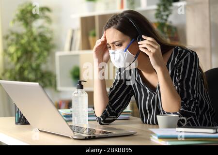 Un tristemente telemarketer che guarda un notebook che indossa una maschera in quarantena con il covid-19 lavorando a casa Foto Stock