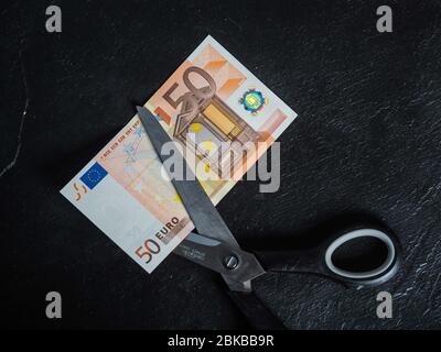 Riduzione delle emissioni e del debito evitando la perdita di valore. Euro moneta moneta inserita in un paio di forbici Foto Stock