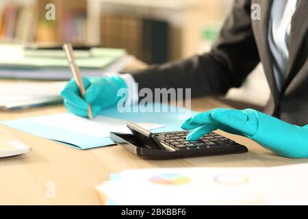 Primo piano di mani bookkeeper calcolo assegno bancario con calcolatrice evitando coronavirus con guanti in lattice seduto a casa Foto Stock