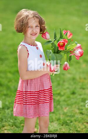 Il bambino in giardino regala un bouquet di tulipani rossi per la festa della mamma Foto Stock