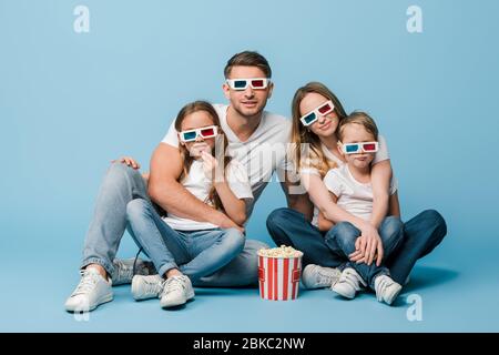 buon film di visione in famiglia in occhiali 3d con secchio di popcorn su blu Foto Stock