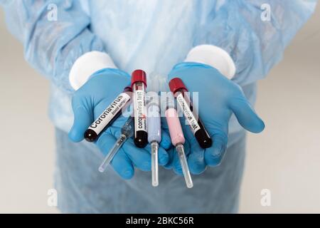 Vista tagliata del medico che tiene provette con campioni di sangue e lettere di coronavirus e siringhe isolate in grigio Foto Stock