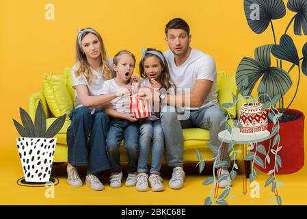 sorpresi film di visione di famiglia su divano con secchio di popcorn su giallo, illustrazione delle piante Foto Stock