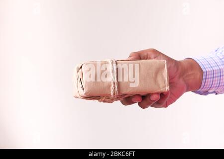 mano dell'uomo che tiene la scatola regalo contro il muro. Foto Stock