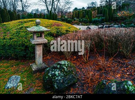 Vista di una tradizionale lanterna in pietra ishi-doro circondata da massi decorativi e cespugli in un giardino giapponese a Bonn, Germania . Foto Stock