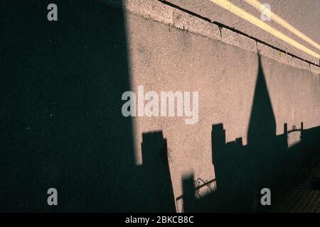 Ombre di un tetto appuntito e porte anteriori su un marciapiede o marciapiede lungo un marciapiede e doppie linee gialle Foto Stock