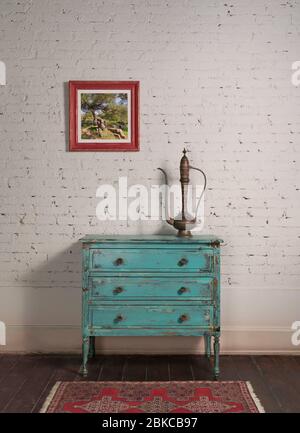 Parete in mattoni bianchi con teiera in rame antico sulla sommità di elegante e squallido armadio in turchese vintage e dipinto appeso in soggiorno Foto Stock