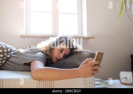 Giovane donna utilizza lo smartphone nel letto Foto Stock