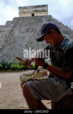 Artigiano che intagliano una maschera da vendere di fronte al tempio di Kukulcan. Il tempio di Kukulcan domina il sito archeologico di Chichen Itza. Foto Stock