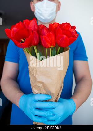 Consegna senza contatto in maschera e guanti monouso di un bouquet di tulipani rossi bello concetto di quarantena e isolamento durante. Panda coronavirus Foto Stock