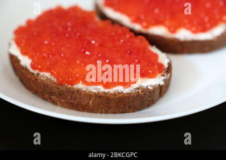 Panini con caviale rosso, burro e pane di segale su piatto bianco, fuoco selettivo. Piatti tradizionali russi Foto Stock