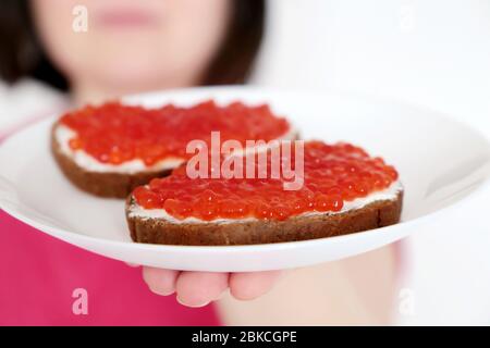 Panini con caviale rosso e burro su piatto bianco in mano femminile. Piatti tradizionali russi, cibo delizioso Foto Stock