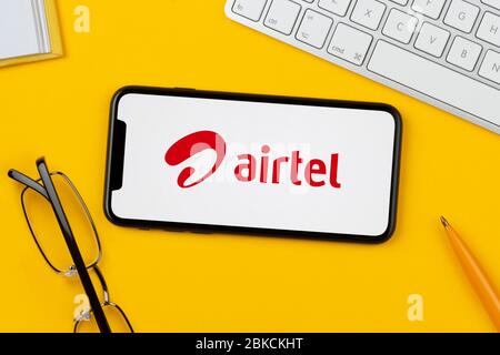 Uno smartphone con il logo Bharti Airtel è appoggiato su uno sfondo giallo insieme a tastiera, occhiali, penna e libro (solo per uso editoriale). Foto Stock