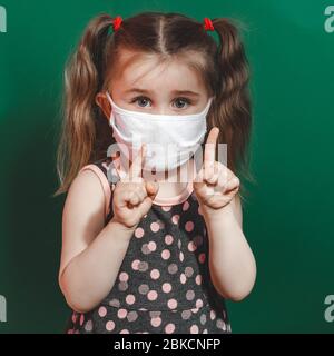 Foto concettuale di bambina in maschera medica che mostra il dito puntato su sfondo verde primo piano 2020 Foto Stock