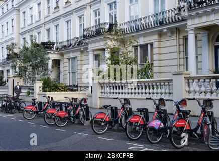 Bici Santander rosse in affitto parcheggiate fuori case bianche a South End di Pembridge Gardens, di fronte a North, Notting Hill, West London, Inghilterra, Regno Unito Foto Stock