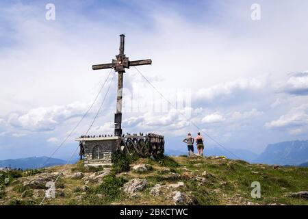 Coppia irriconoscibile di fronte alla croce religiosa sulla vetta del Monte Sonntagskogel nelle Alpi, nel quartiere Sankt Johann im Pongau, Austria Foto Stock