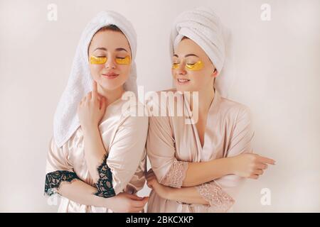 Due giovani sorelle in accappatoi con asciugamani sulla testa isolati su sfondo bianco. Spa a casa Foto Stock