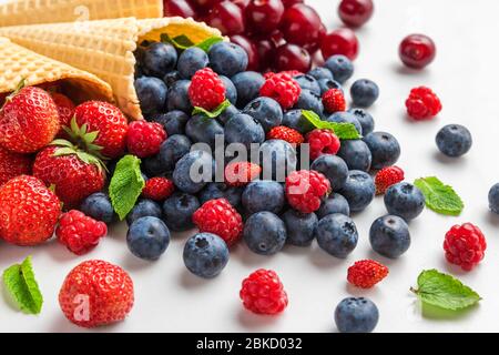 Frutti di bosco freschi estivi con menta in coni di gelato waffle su sfondo di marmo bianco. Concetto di cibo estivo. Foto Stock