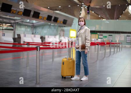 Donna con bagagli si trova presso i banchi di check-in quasi vuoti presso il terminal dell'aeroporto a causa delle restrizioni di viaggio relative alla pandemia di coronavirus/epidemia di Covid-19. Foto Stock