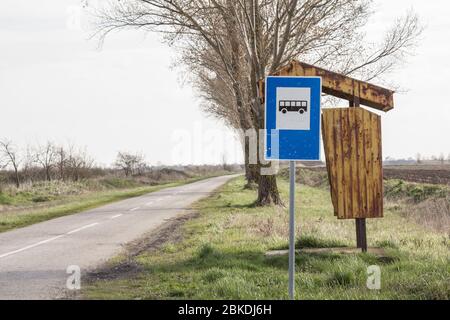 Abbandonata fermata di autobus progetto jugoslavo, di fronte a un paesaggio trascurato campagna e una strada danneggiata in Serbia, in una zona rurale colpito da emigrazione. Pi Foto Stock