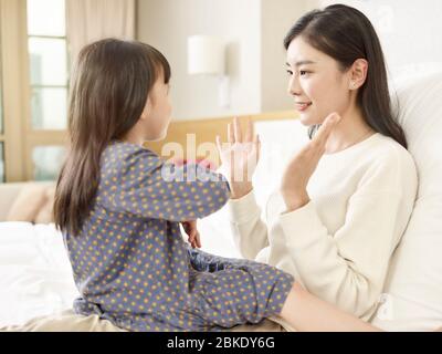 giovane madre asiatica e figlia che hanno una piacevole chiacchierata seduta sul letto a casa Foto Stock