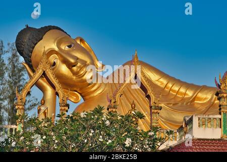In una mattina presto, la luna piena è vista sopra la testa del cosiddetto Buddha "a strisciamento" di Wat si Sunthorn lungo 29 m a Thalang, Phuket, Thailandia Foto Stock