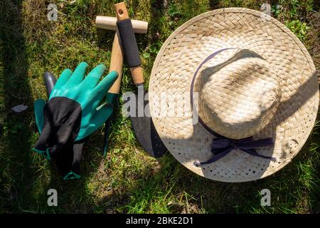 Cappello da sole con guanti e attrezzi da giardinaggio adagiato su un prato verde in un giardino primaverile al sole concettuale delle stagioni viste dall'alto in basso Foto Stock