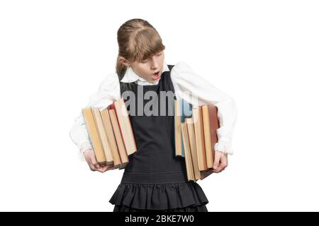 ragazza sorpresa in uniforme scolastica porta due pile di libri sotto ascelle isolato su sfondo bianco Foto Stock