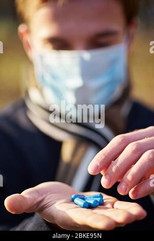 Un ragazzo in una maschera medica tiene le mani con pillole alla macchina fotografica. Foto di concetto sulla pandemia Covid 19 Foto Stock