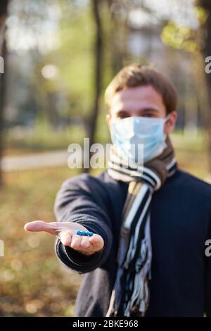 Un ragazzo in una maschera medica tiene le mani con pillole alla macchina fotografica. Foto di concetto sulla pandemia Covid 19 Foto Stock