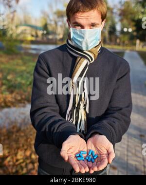 Un ragazzo in una maschera medica tiene le mani con pillole alla macchina fotografica. Foto di concetto sulla pandemia Covid 19 Foto Stock