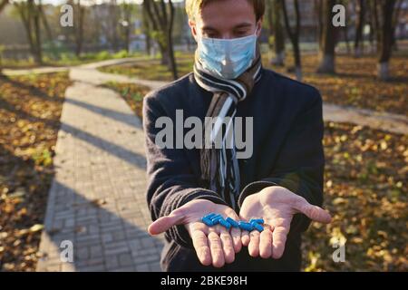 Un ragazzo in una maschera medica tiene le mani con pillole alla macchina fotografica. Foto di concetto sulla pandemia Covid 19 Foto Stock